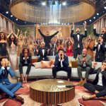 High-definition, realistic image capturing an unexpected twist in a generic reality TV show 'House of Stars'. The setting should include a beautifully decorated living area of a television set, with various contestants showing a wide range of emotions: shocked, jubilant, and dismayed. Perhaps some have their hands on their heads, while others are applauding, creating a dramatic atmosphere. No specific celebrities or real persons should be depicted, just generic contestants.